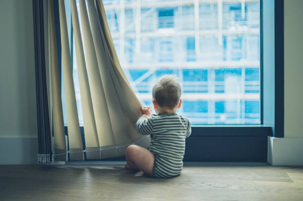A little baby is playing with the curtain in a high rise apartment